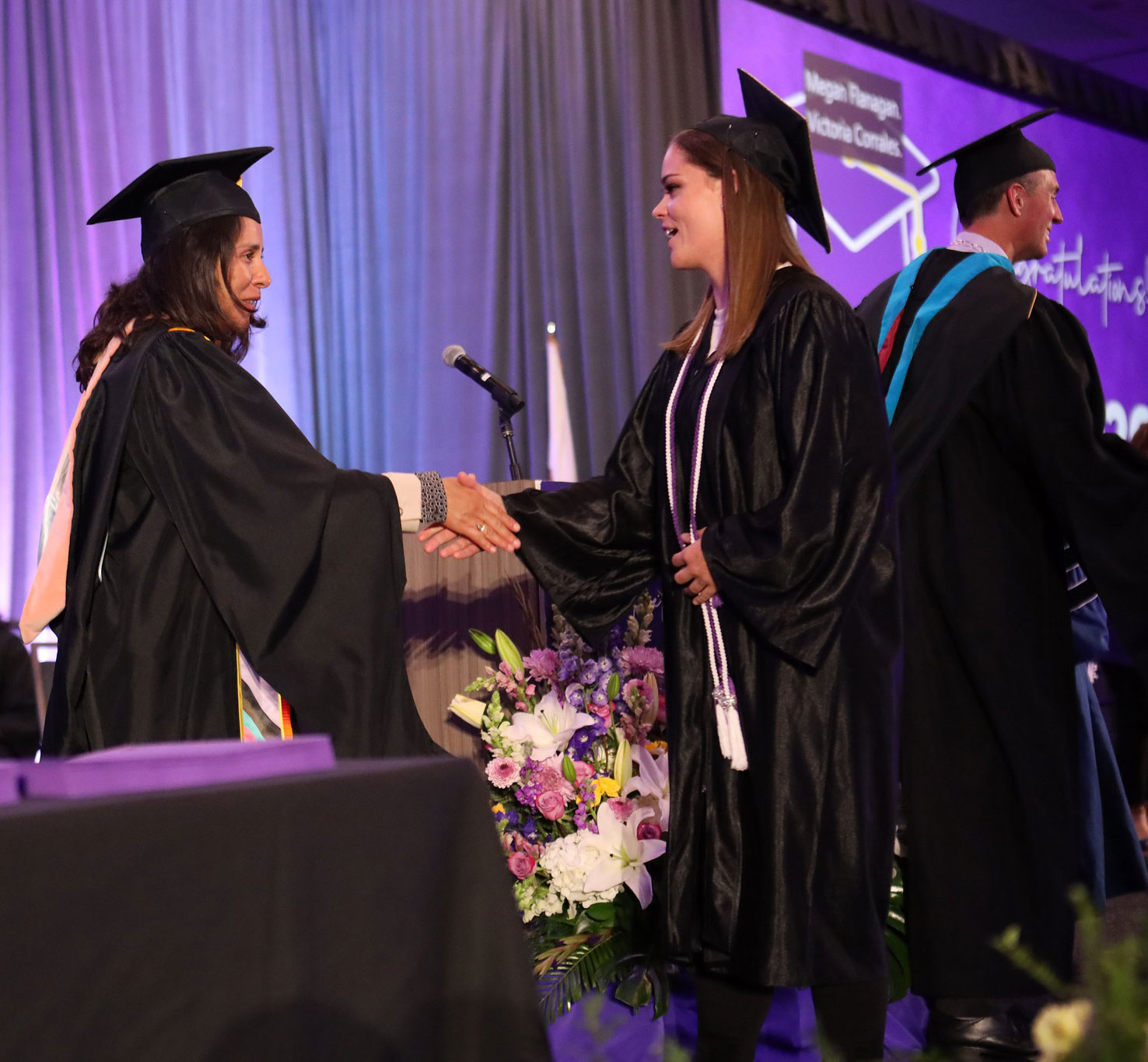 Trustee Geysil Arroyo shakes a graduate's hand on stage.