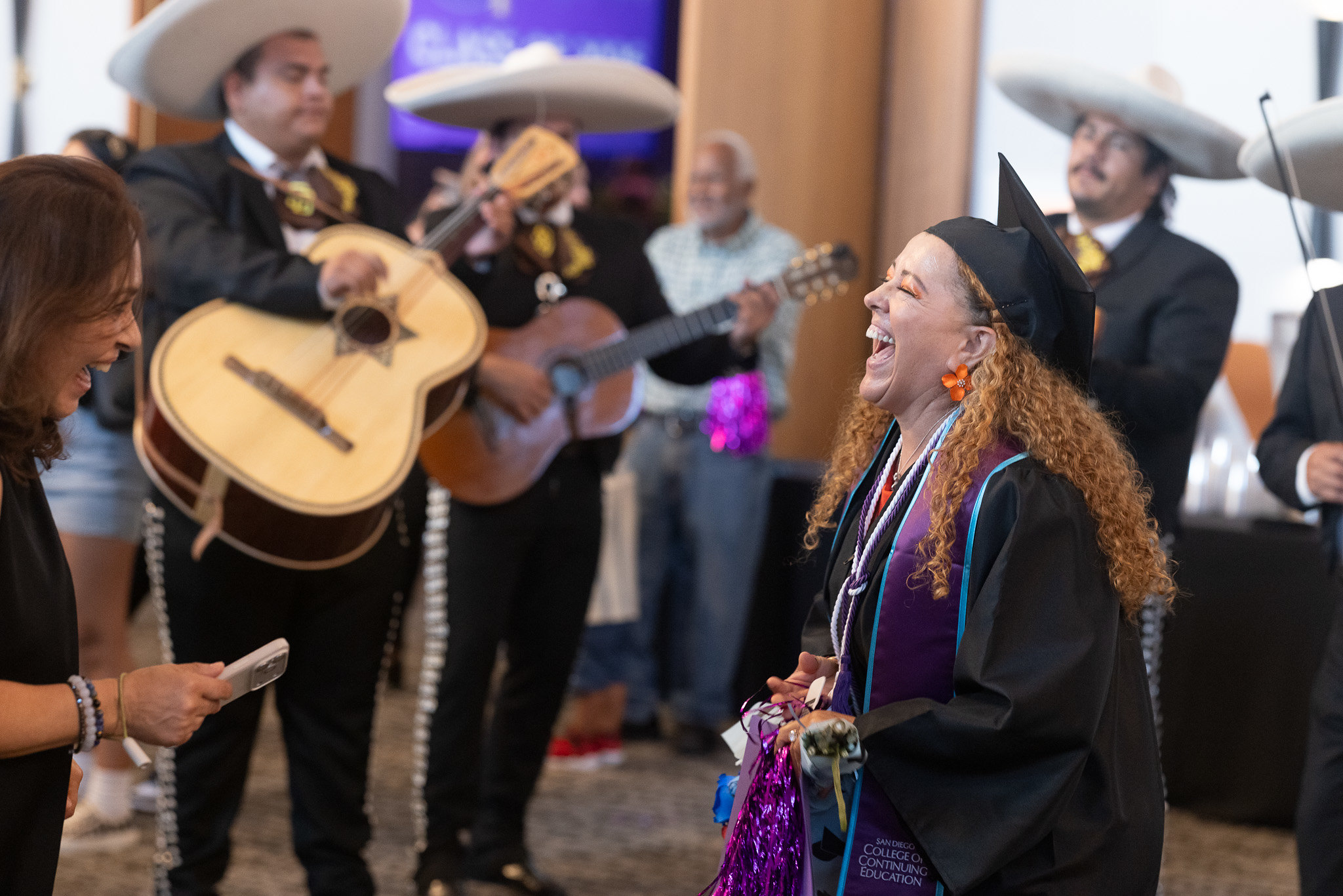 A graduate in the lobby laughing. A mariachi band plays in the background.