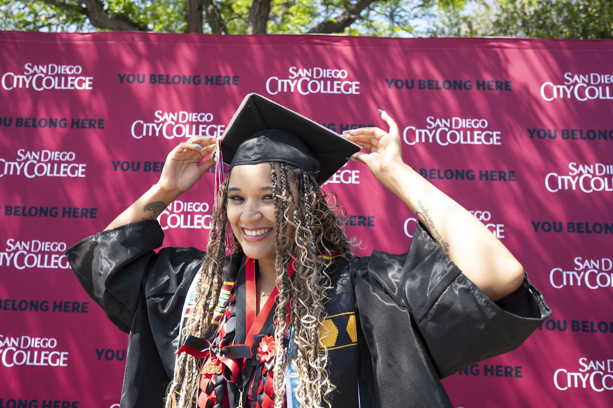 A graduate smiles while adjusting her cap.&nbsp;