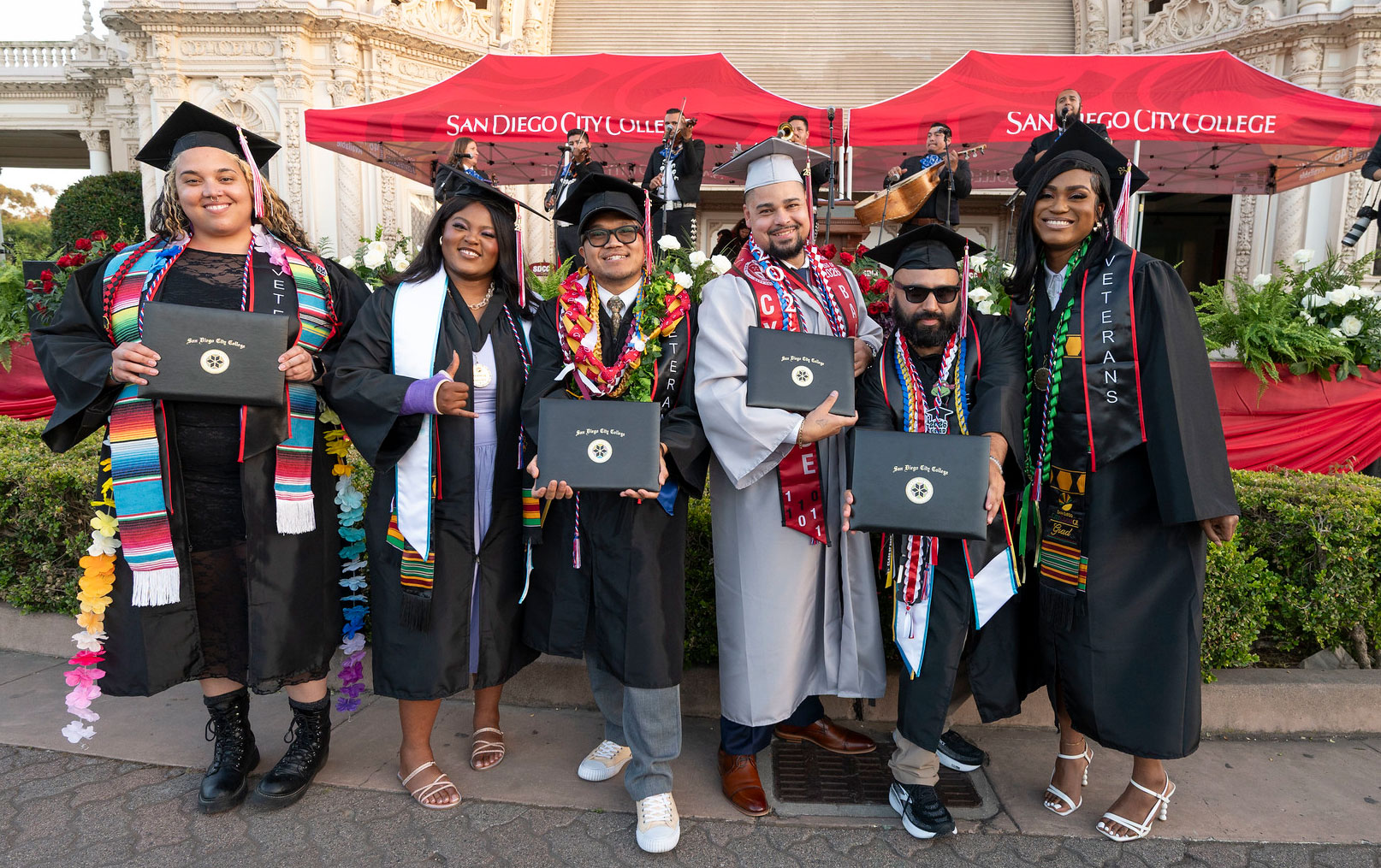 Six students in graduation caps and gowns hold up their degrees.&nbsp;