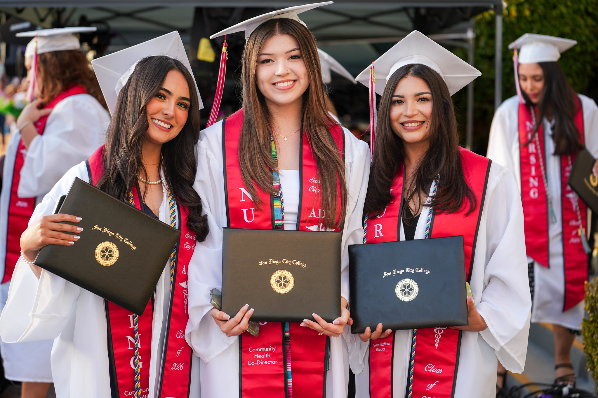 Three graduates from City College's nursing program hold up their degrees.
