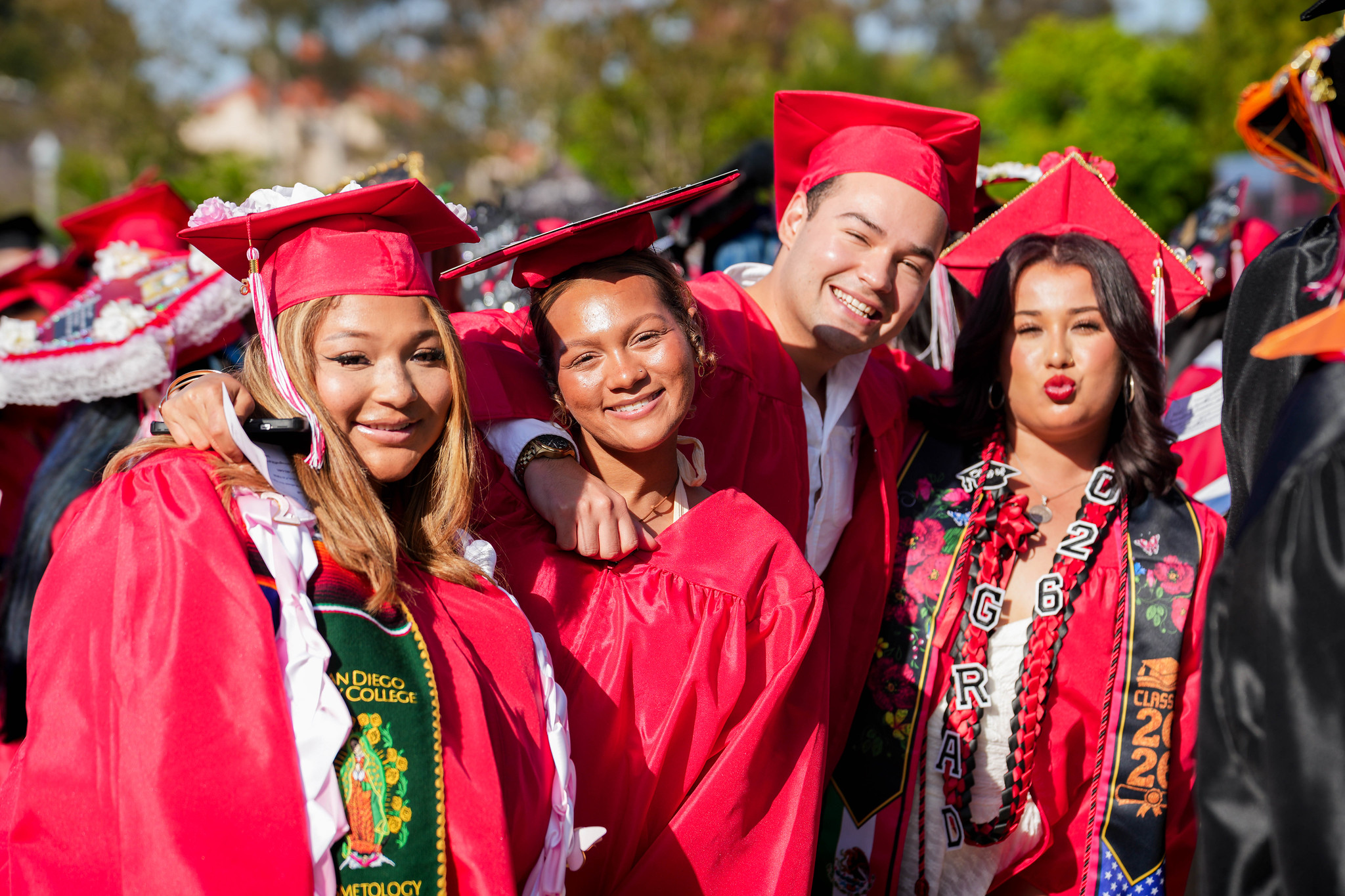 Four graduates in red caps and gowns pose at commencement.