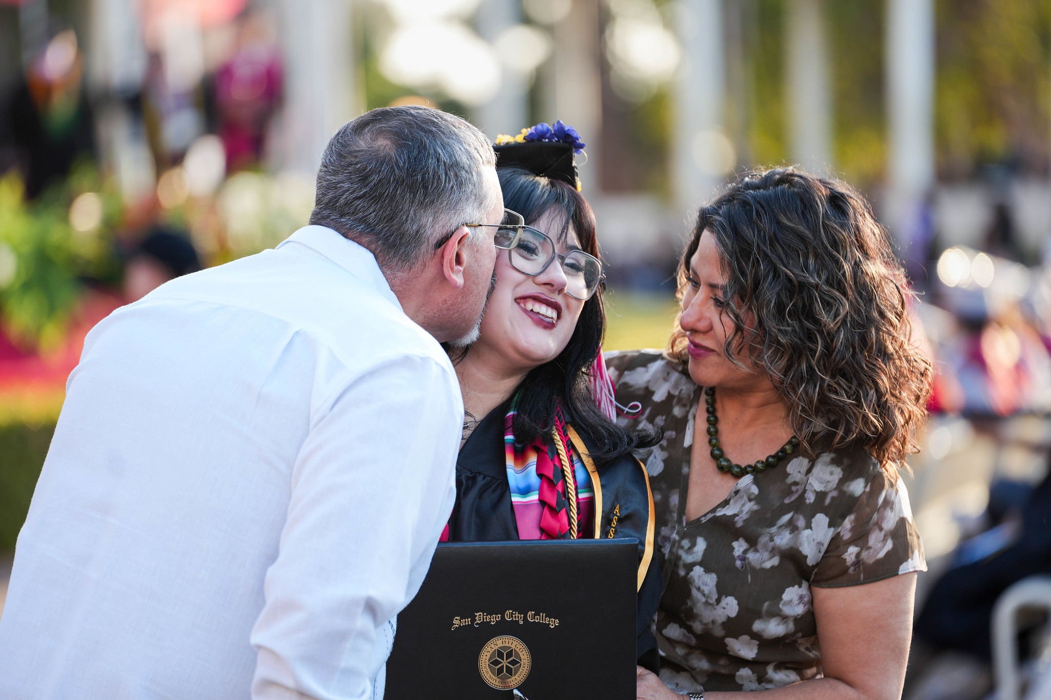 A graduate gets a kiss on the cheek from a proud family member.&nbsp;
