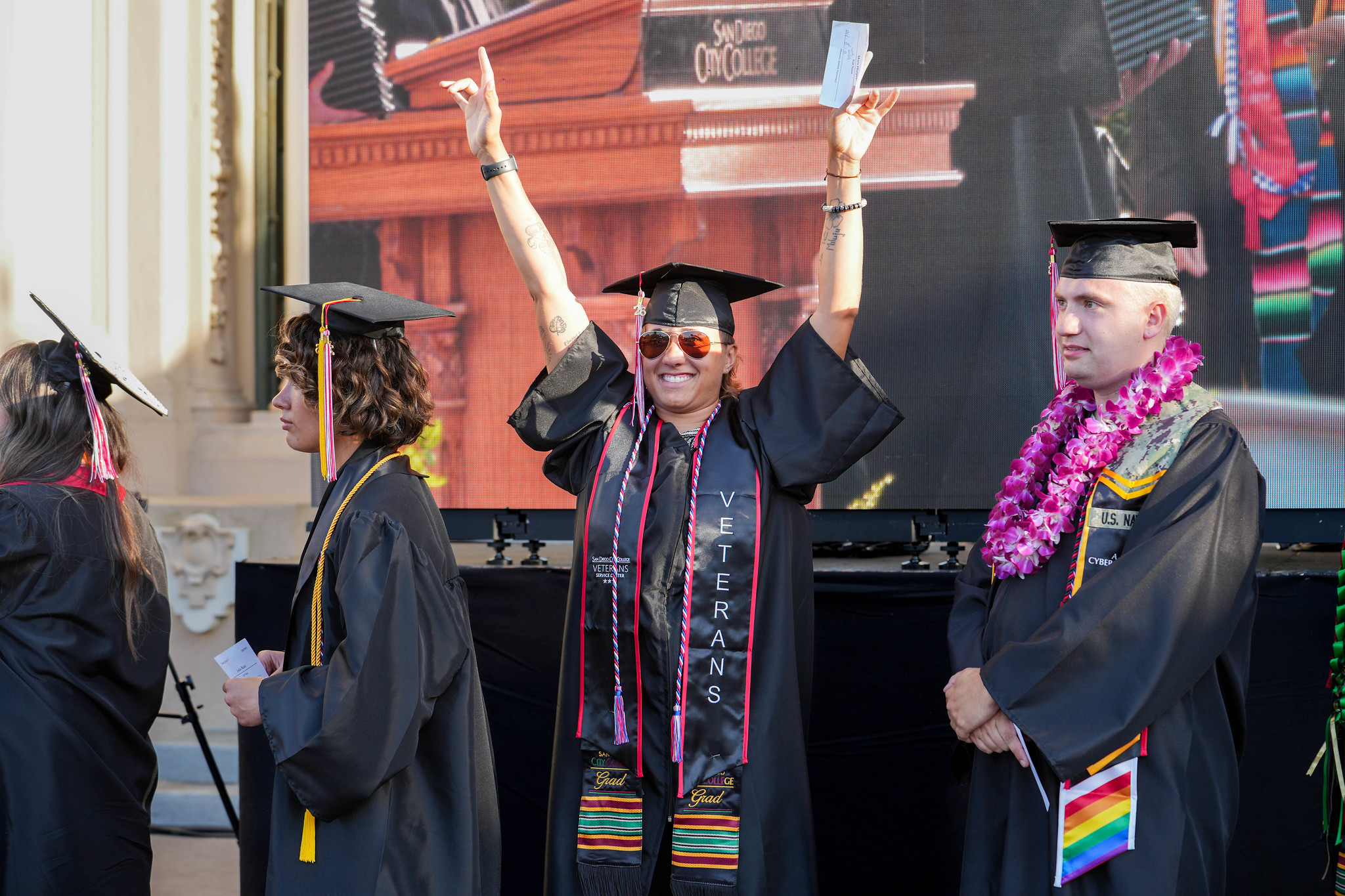 A graduate with both hands in the air gestures to the audience in celebration while waiting in line to get his degree.&nbsp;