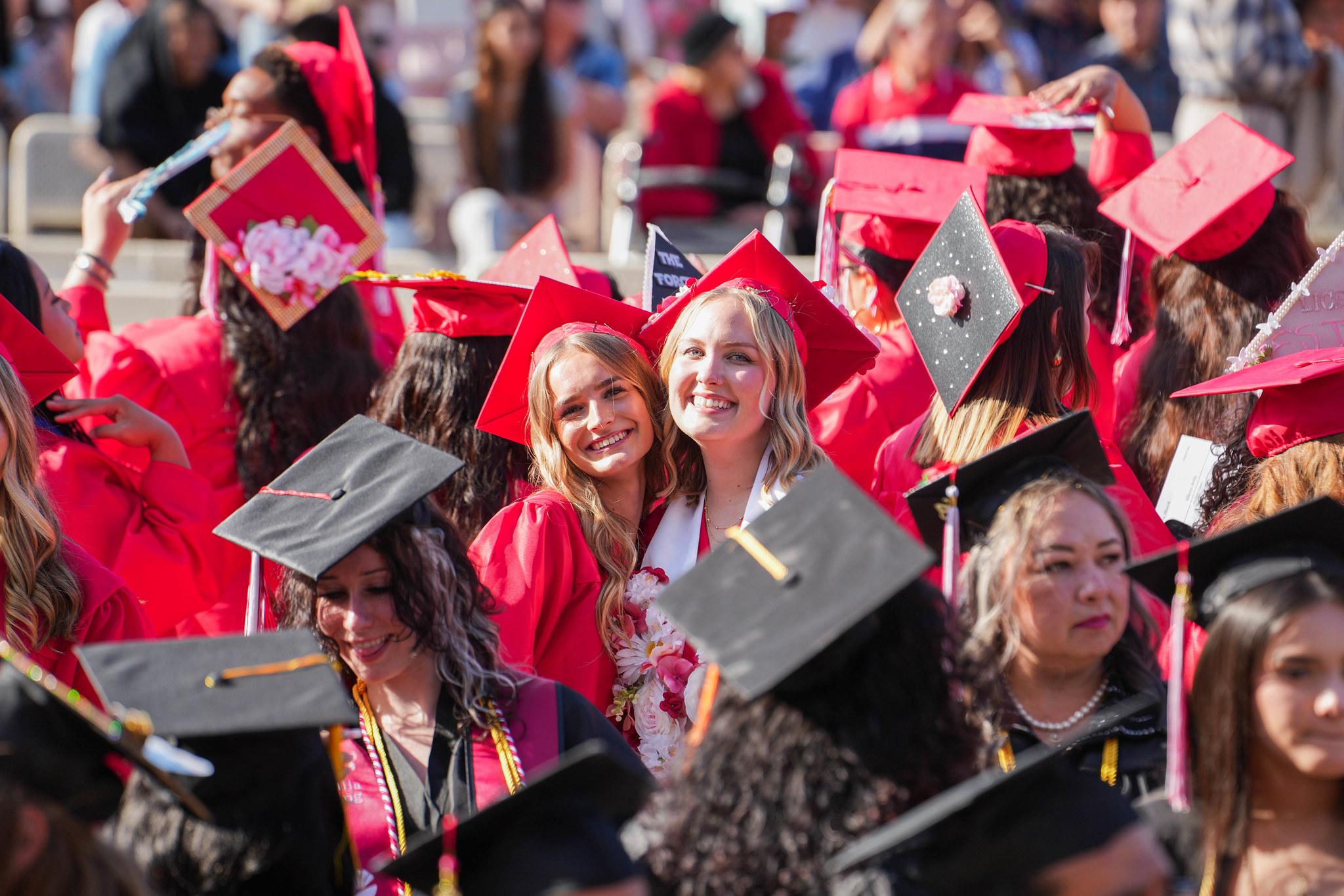 Two grads pose together surrounded in the audience by the other graduates.&nbsp;