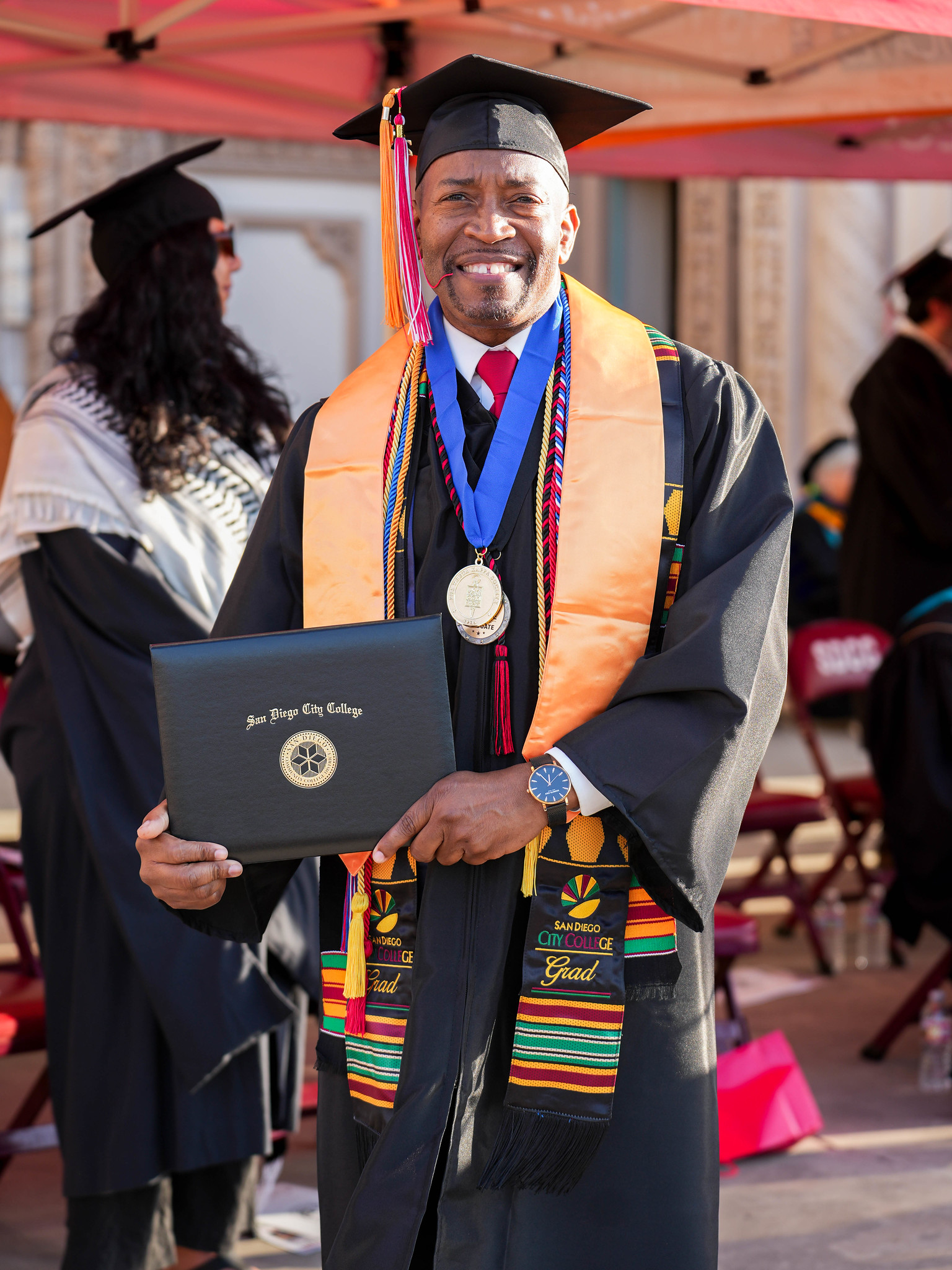 A graduate on stage smiling with his degree.&nbsp;