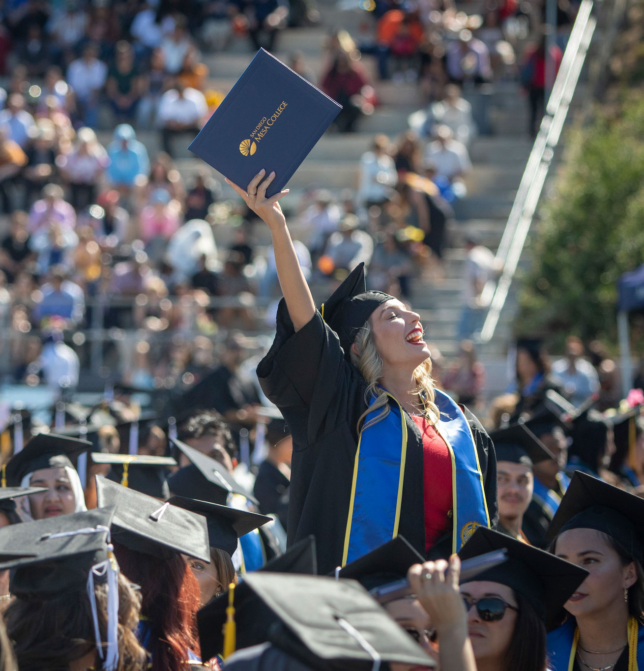 A grad in the audience holds her degree up in the air.&nbsp;