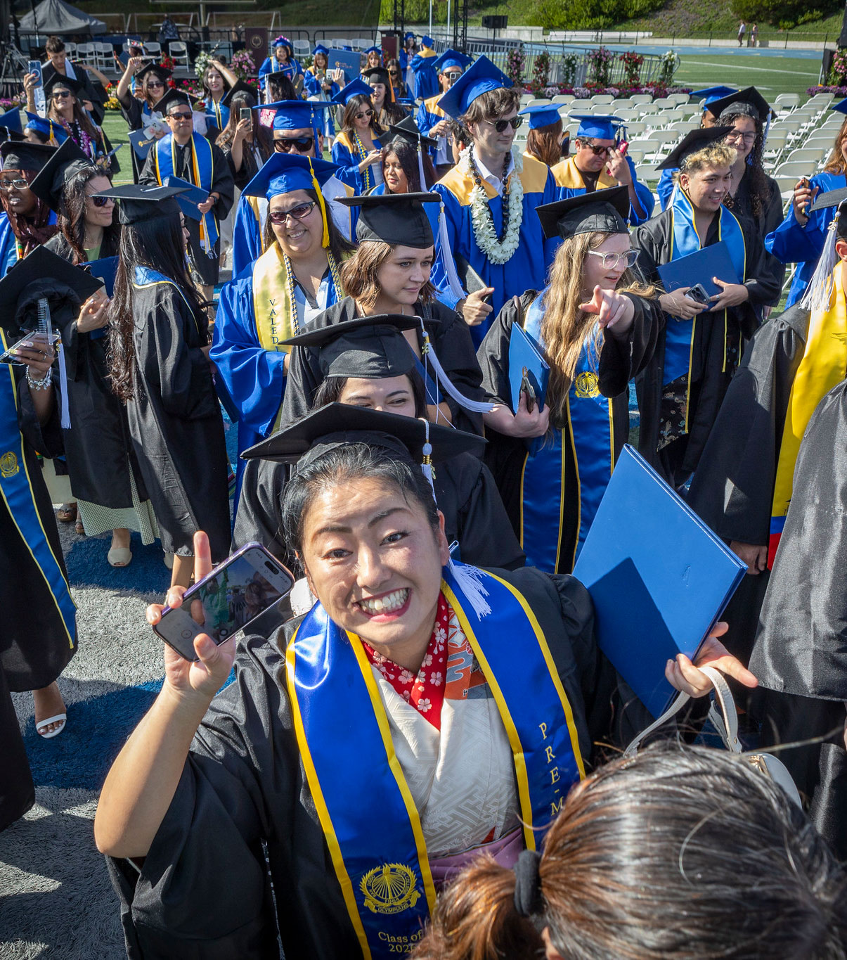 A grad with her degree smiles and waves to the camera.