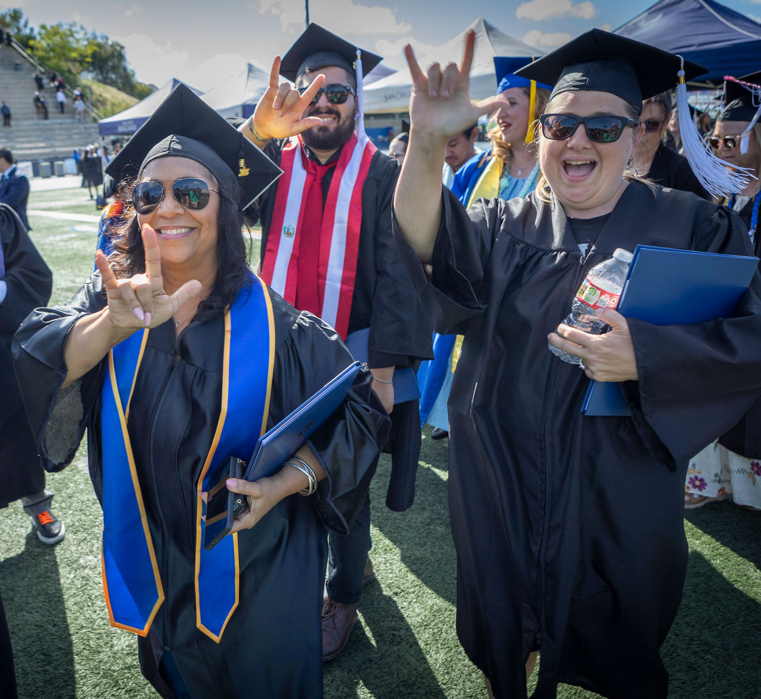 Three grads give the I love you sign with their hands.