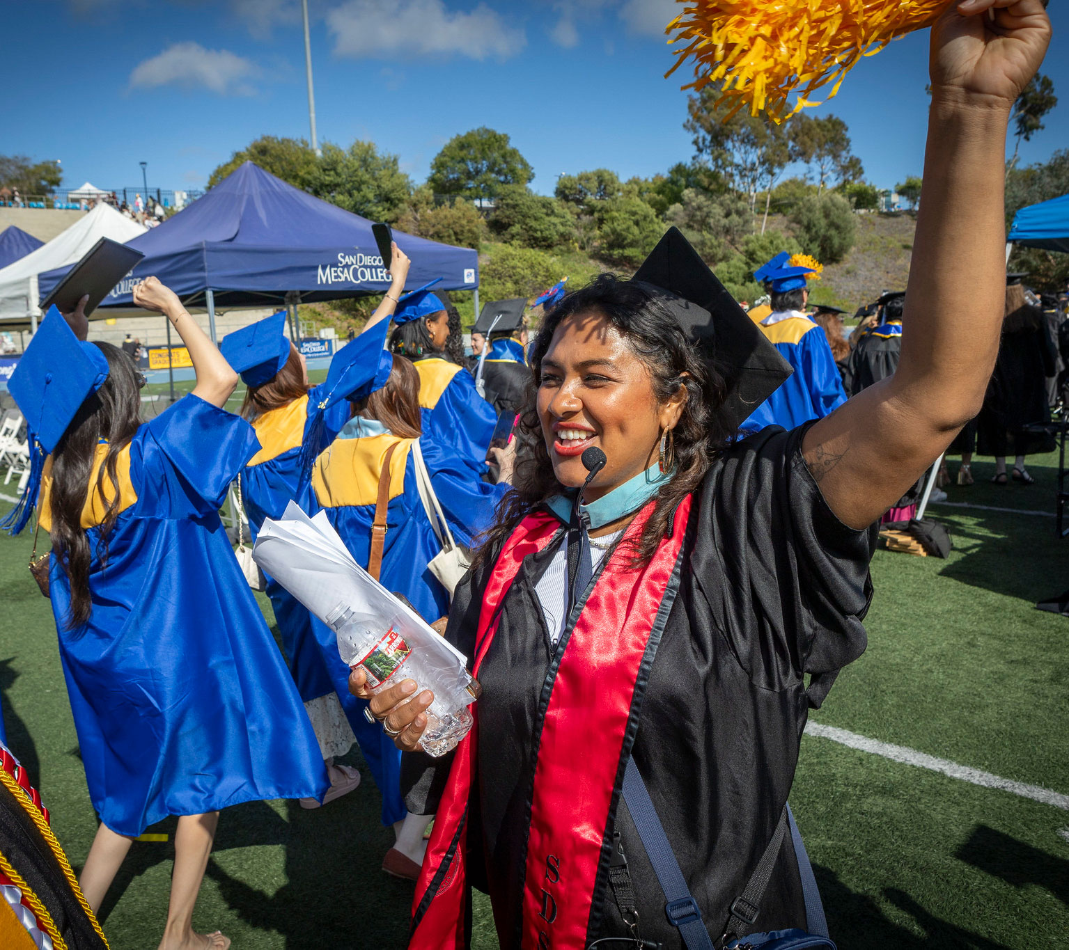 A grad cheers with a gold pom pom.