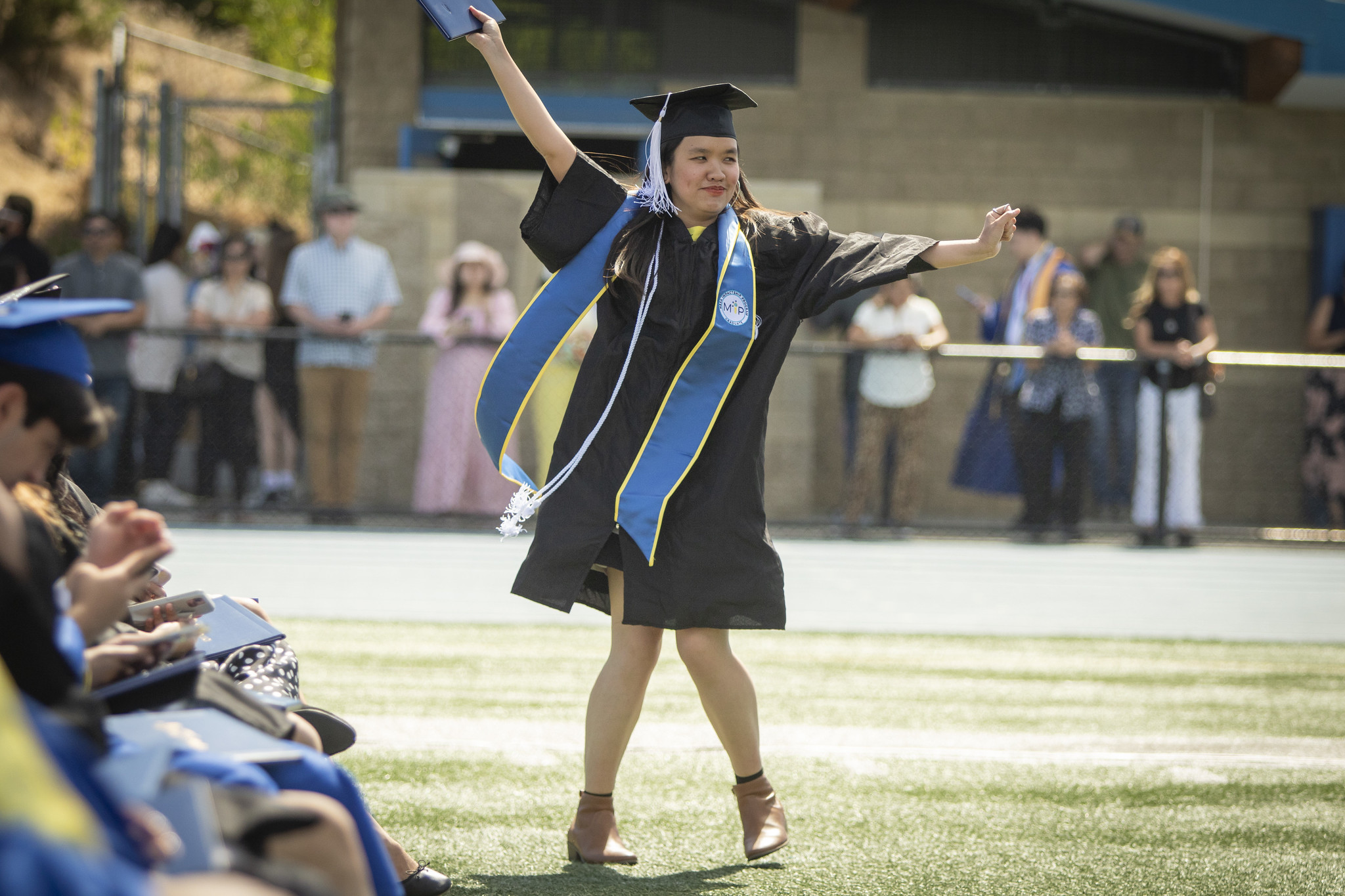 A student spreads her arms out, holding her degree in celebration.&nbsp;