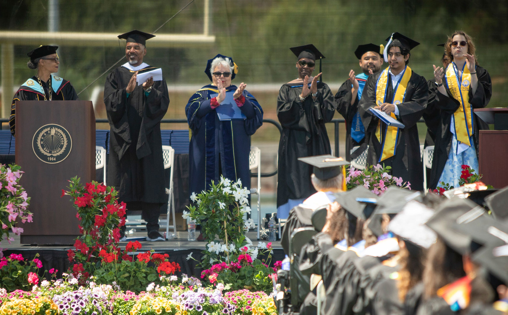 Faculty members on stage clap while Mesa President Ashanti Hands speaks at a podium.&nbsp;