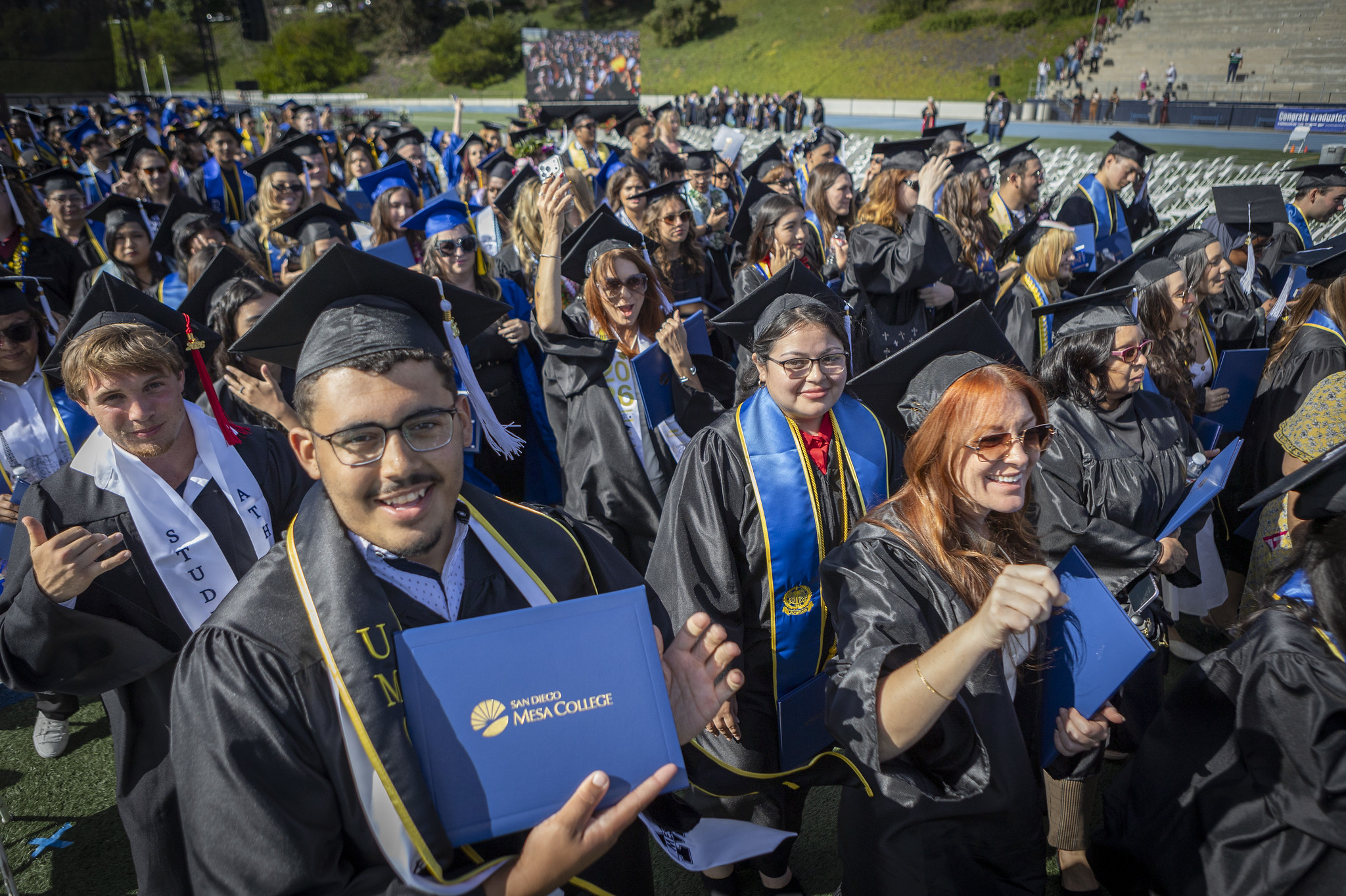 Graduates in the audience hold up their degrees.