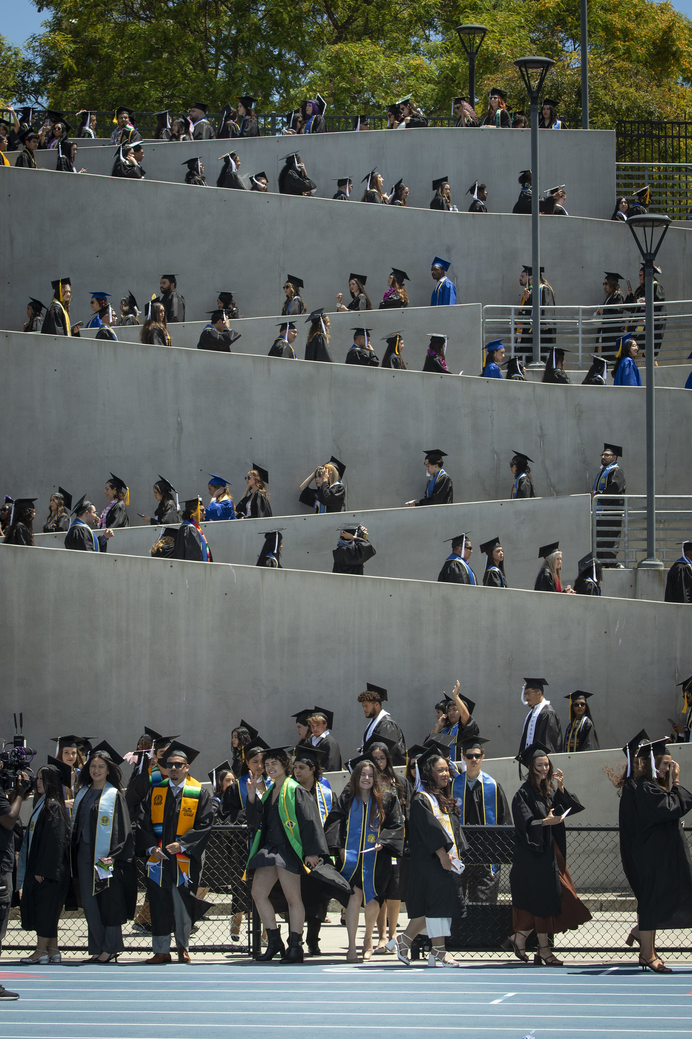 Graduates form a zig zag as they walk down the stadium ramp toward the grass field.&nbsp;&nbsp;