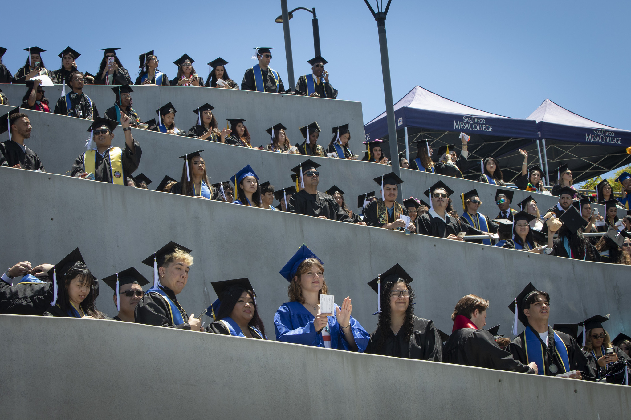 Graduates form a zig zag as they walk down the stadium ramp toward the grass field.&nbsp;&nbsp;