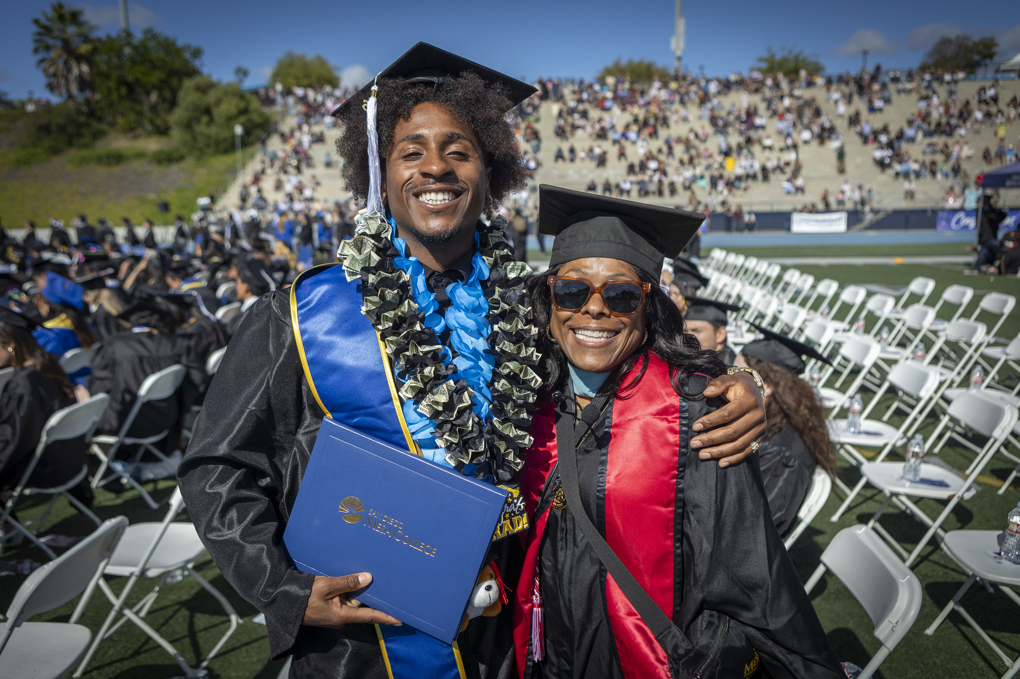 A grad hugging another grad and holding up his degree.&nbsp;