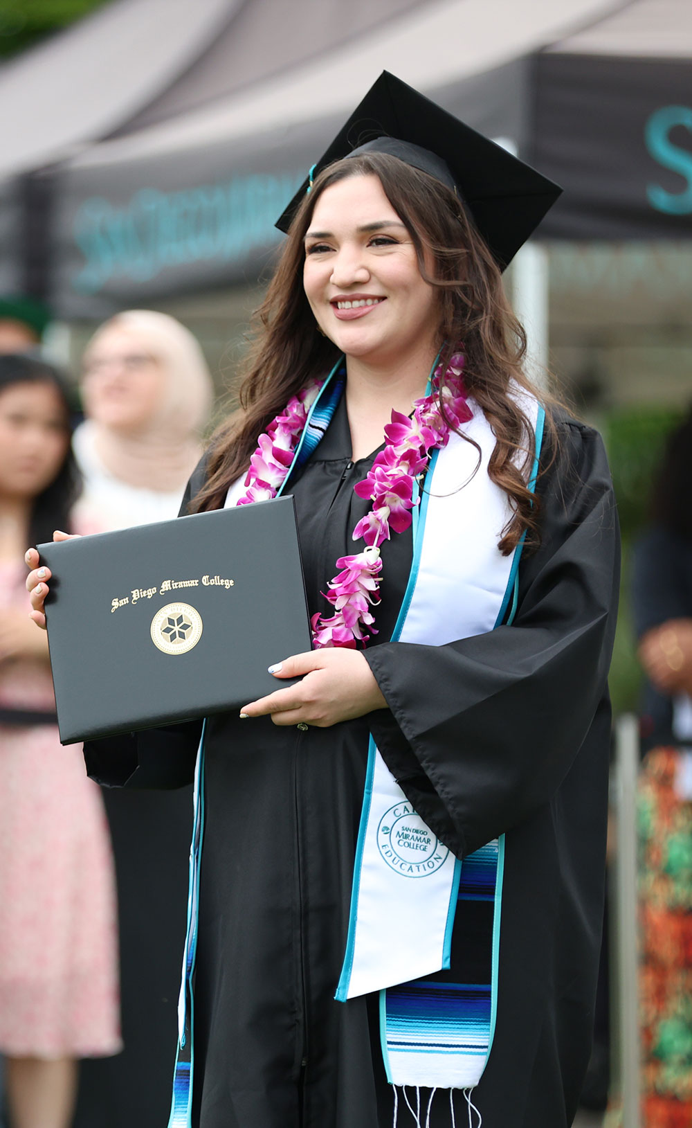 A student holds up their degree at commencement.
