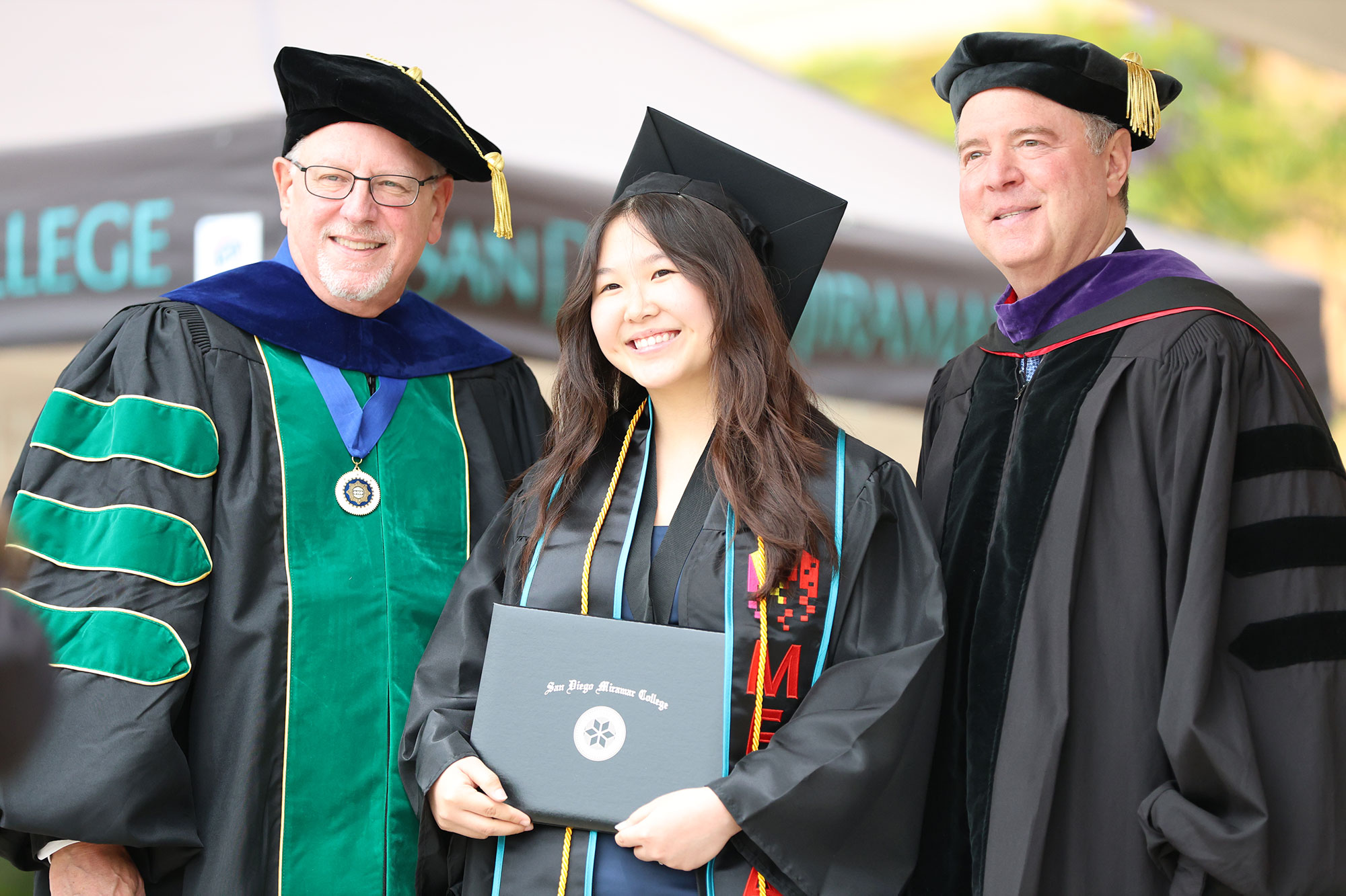 Miramar College President Wes Lundburg and U.S. Senator Adam Schiff on stage with a student receiving her degree at commencement.