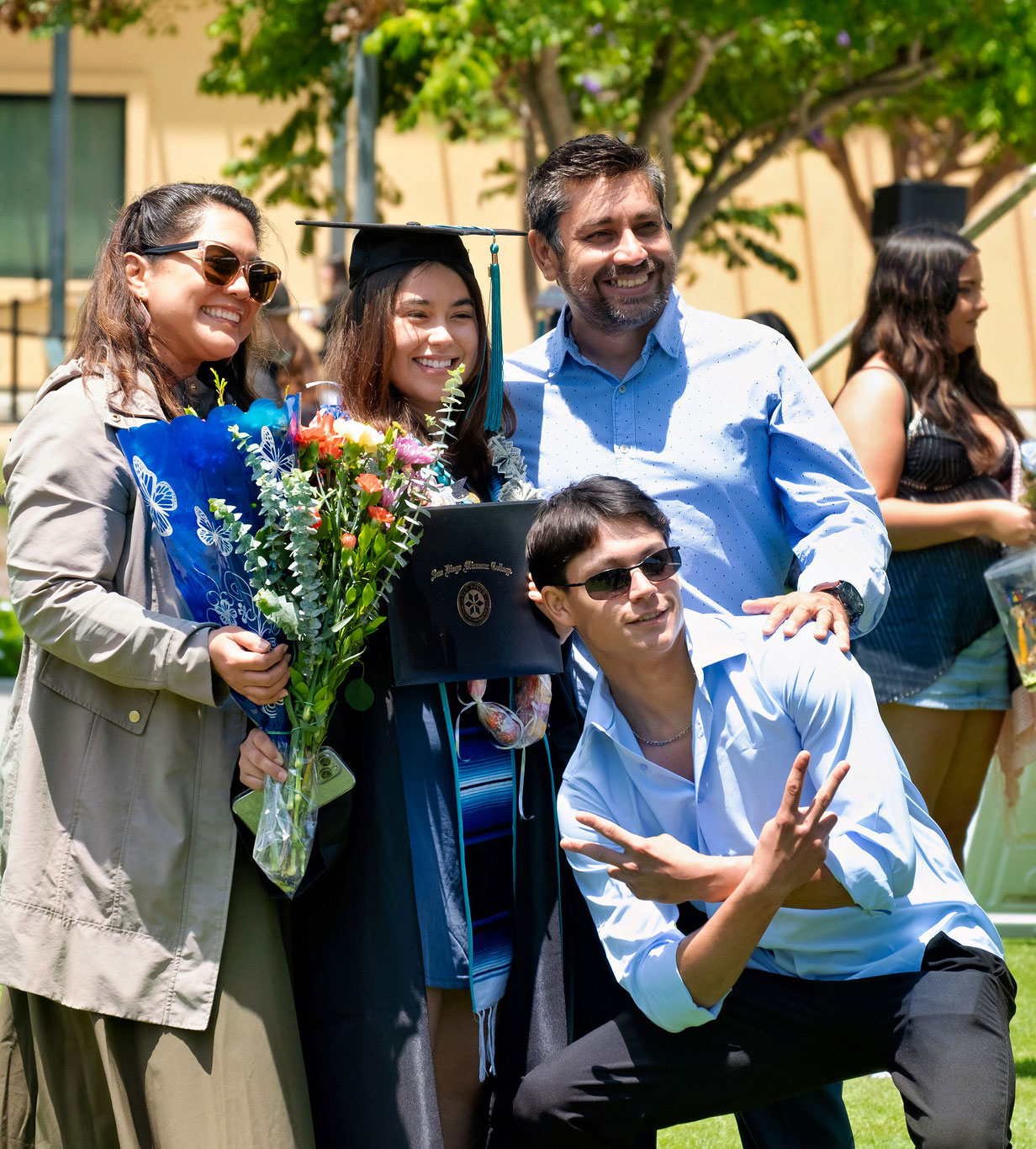 A grad with flowers and her degree takes a pic with 3 family members.