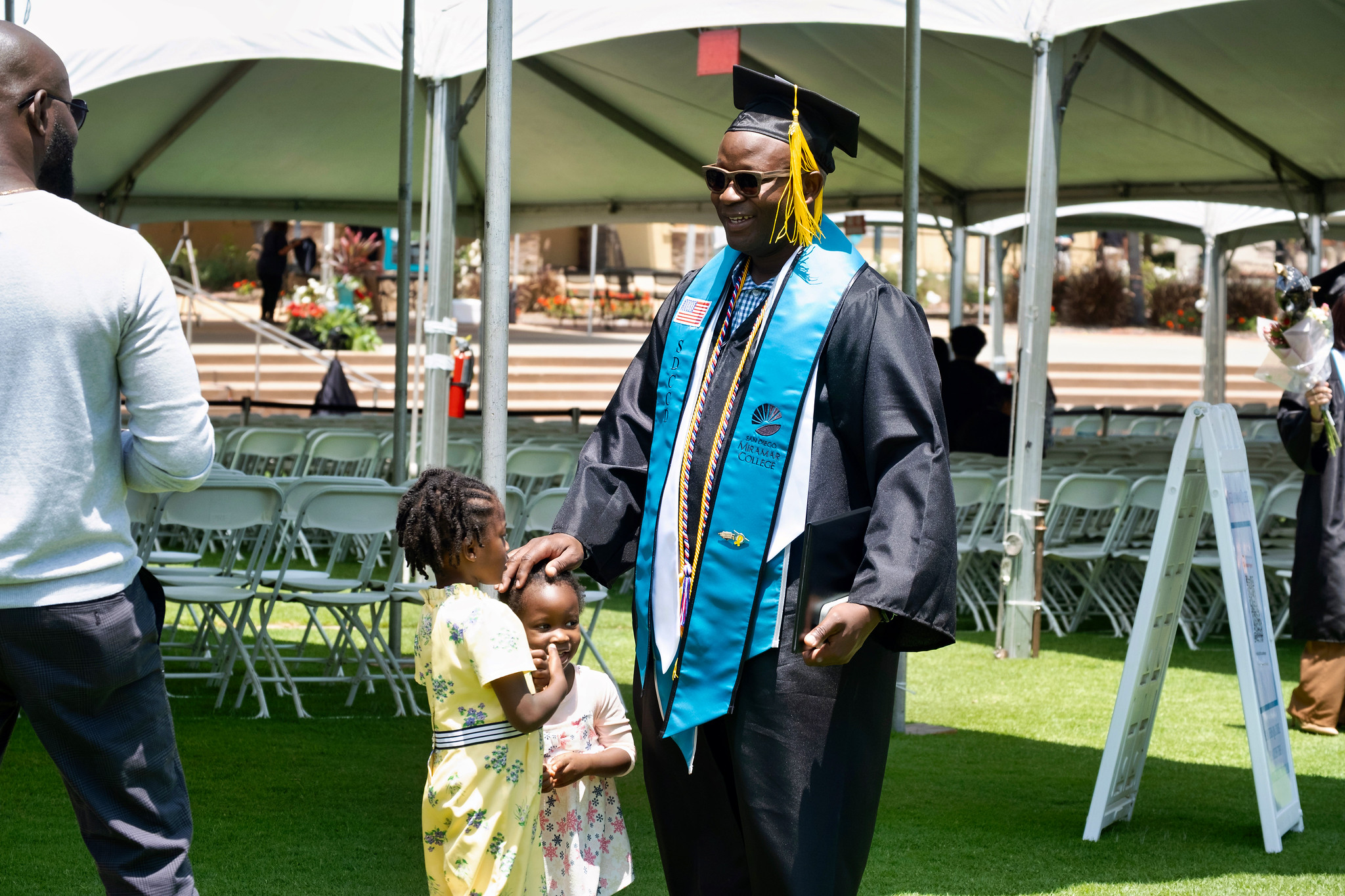 A graduate with two children is smiling an holding his degree.