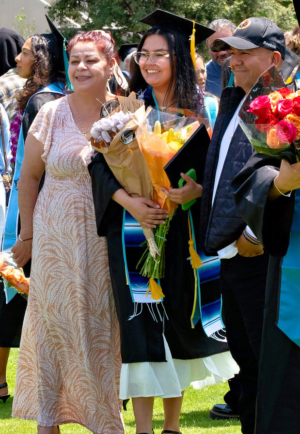 A graduate holding flowers and her degree is taking a photo with two family members.&nbsp;
