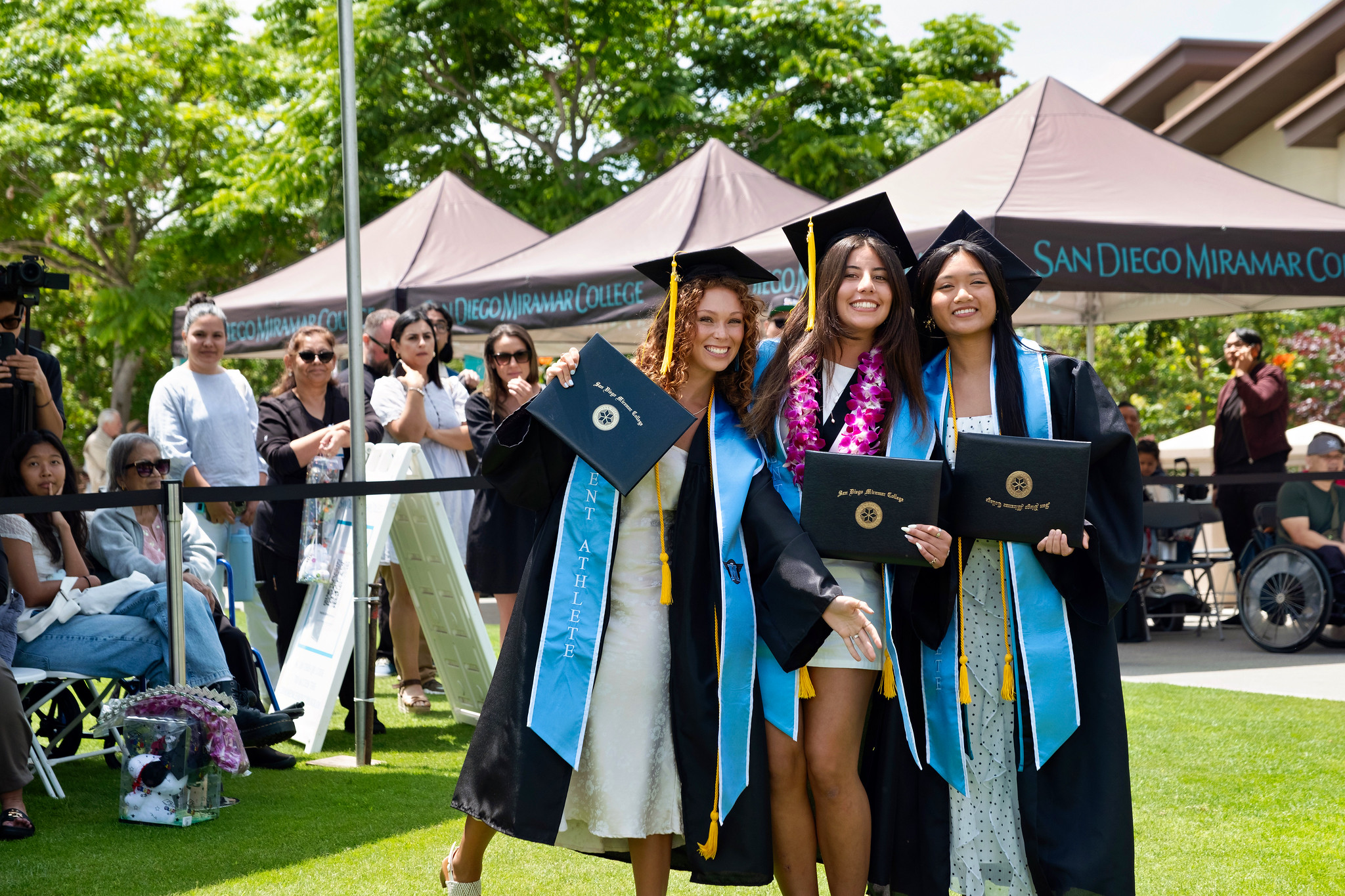 Three graduates hold up their degrees.
