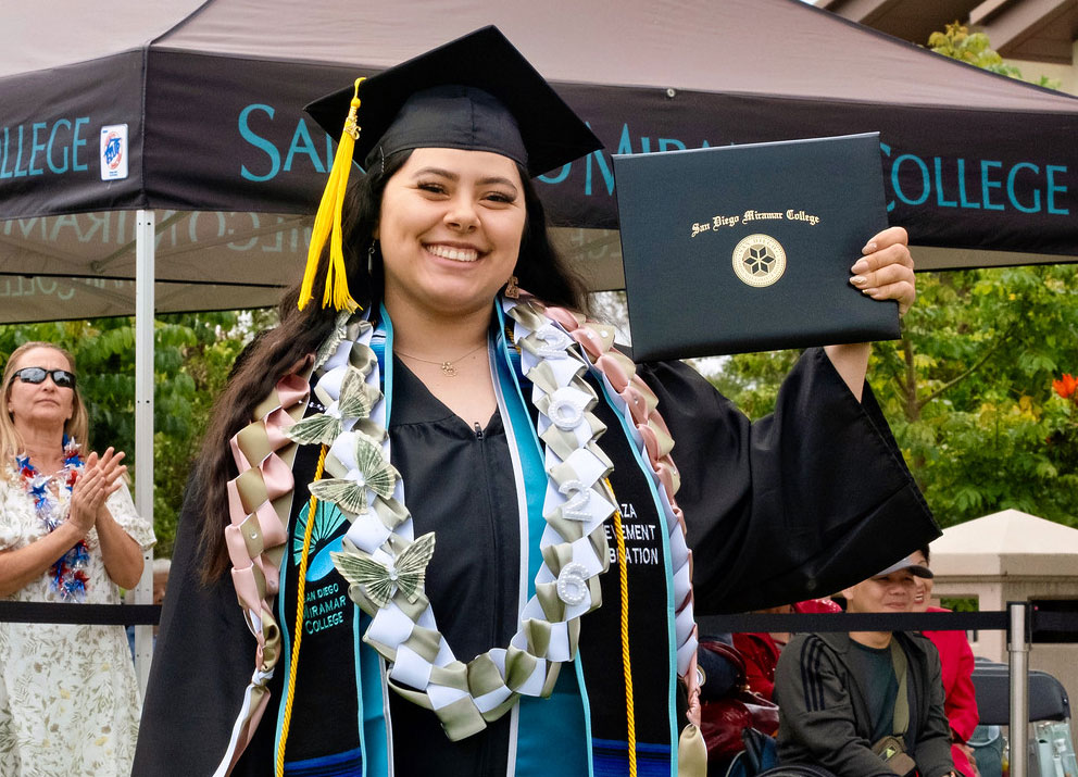 A student holds up their degree.
