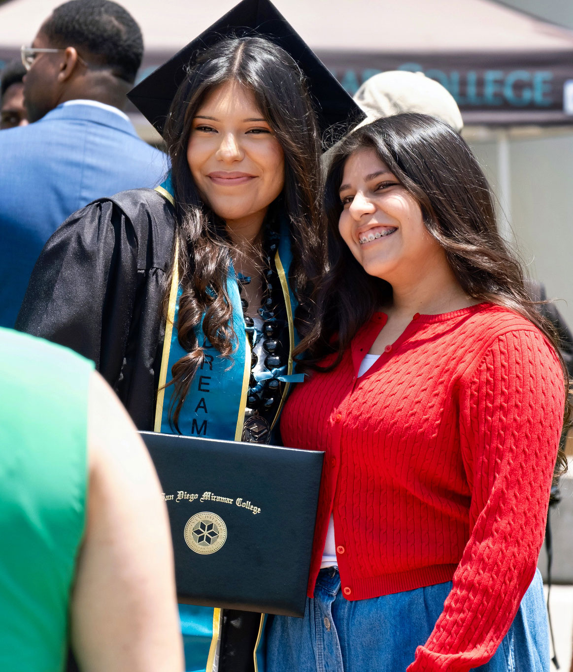 A graduate holding her degree takes a photo with a family member.