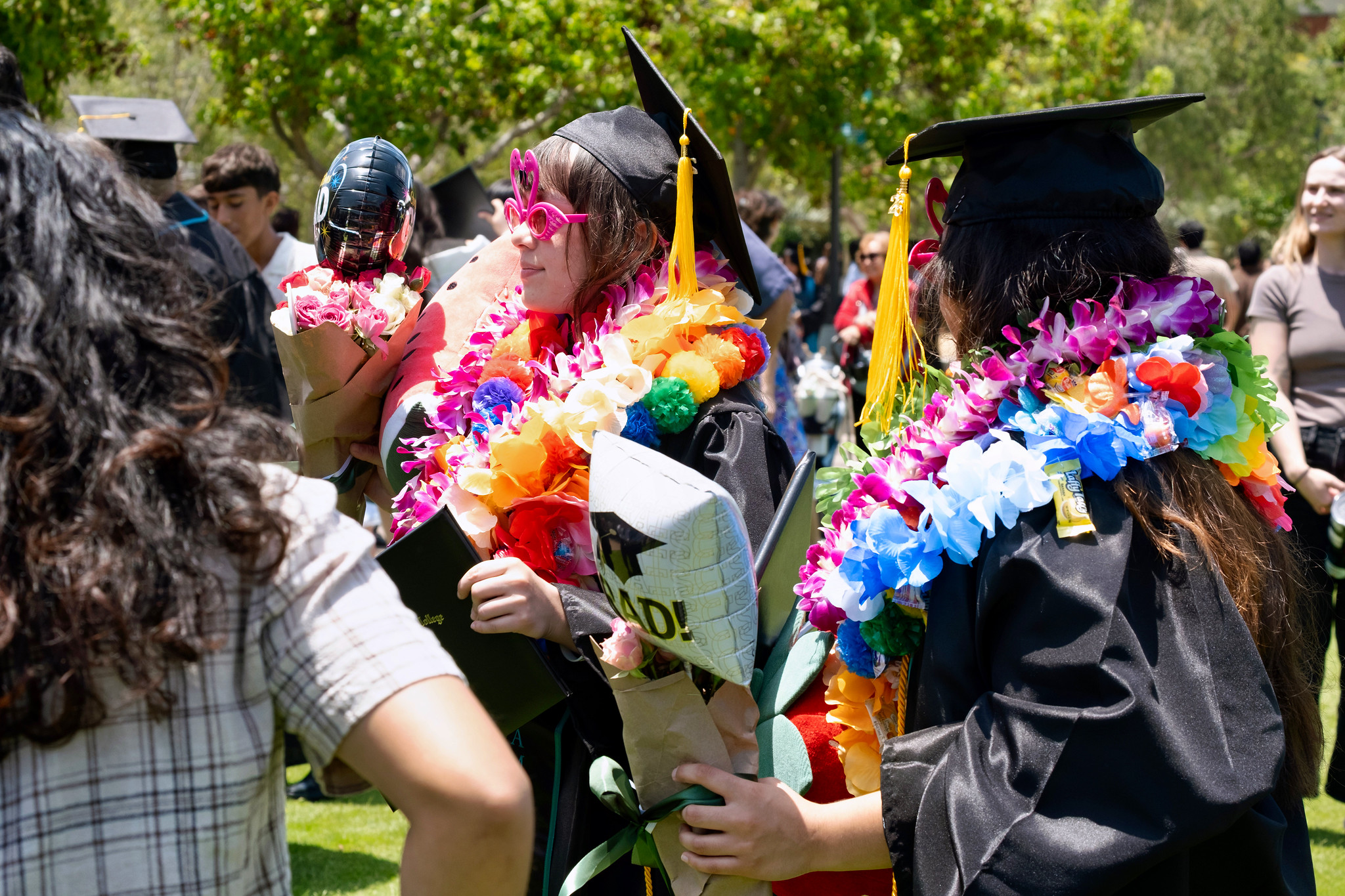 Two graduates in caps and gowns and multiple colorful flower leis.