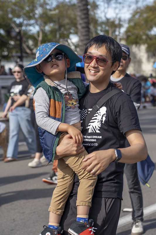 A man carrying a young boy while waking in the parade.