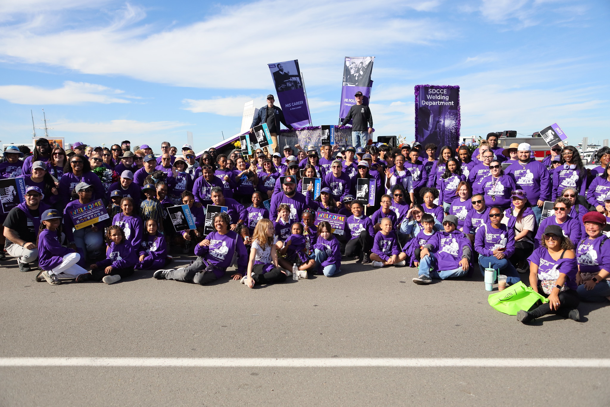 About 100 College of Continuing Education staff and students take a group photo in matching purple shirts in front of their float.