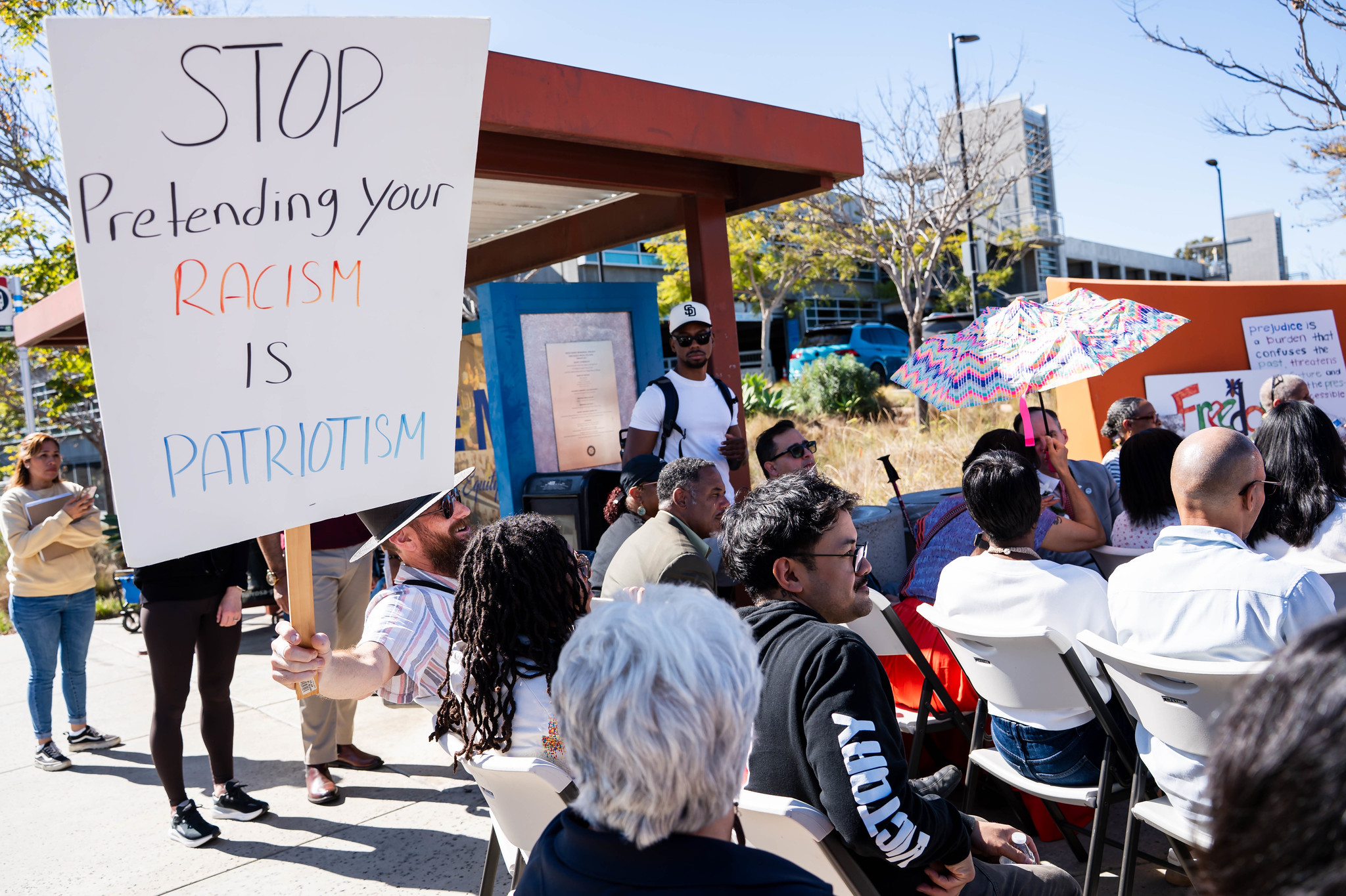 
A man in the audience holds a sign that says stop pretending your racism is patriotism.
