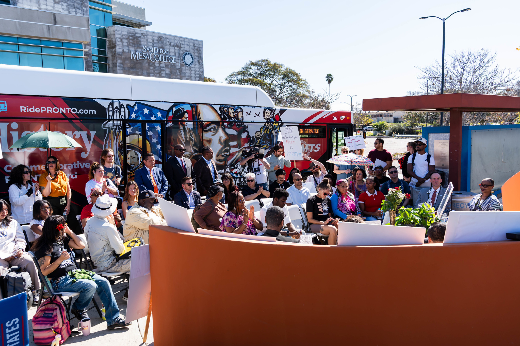 
The audience seated in front of a bus that has a wrap for Black History Month.
