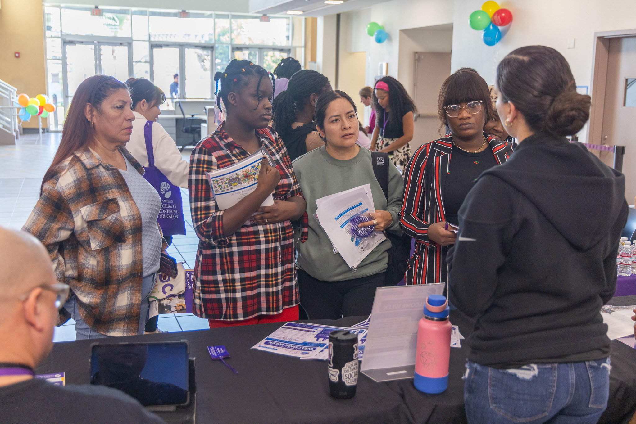 
Four College of Continuing Education students talk to a person at a welcome table.
