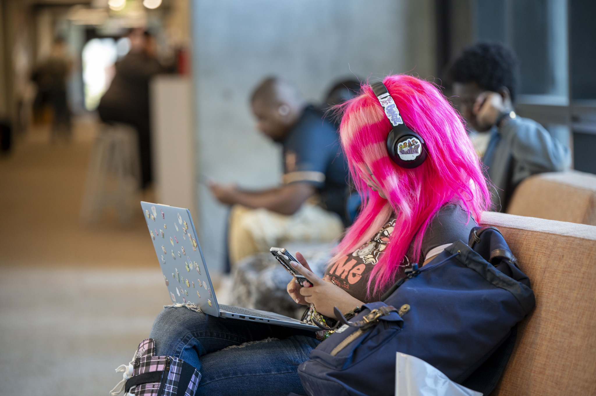 
A student with bright pink hair and headphones seated and looking at her cell phone.
