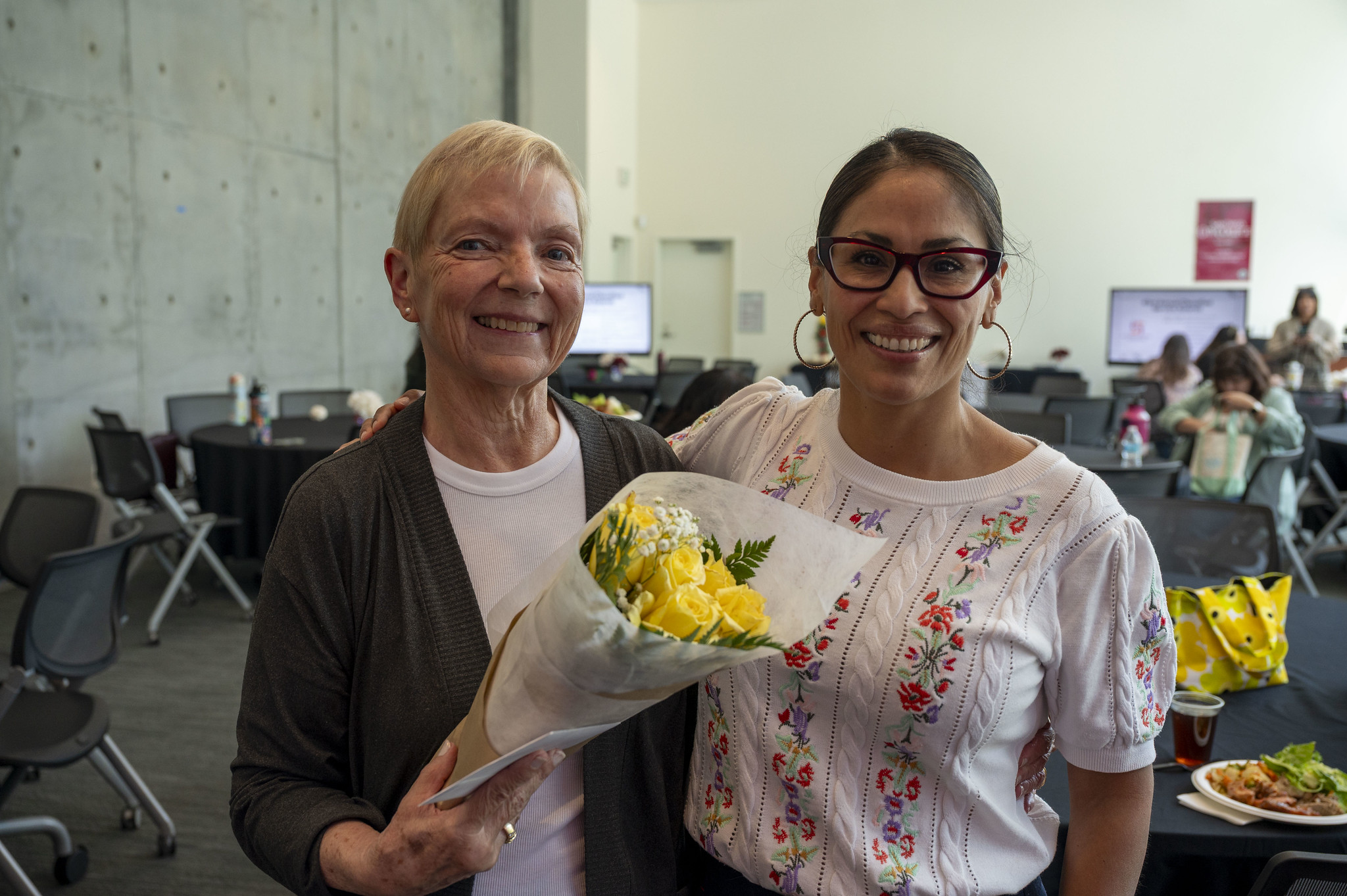 Two ladies at City College's event. One is holding a bouquet of sunflowers.