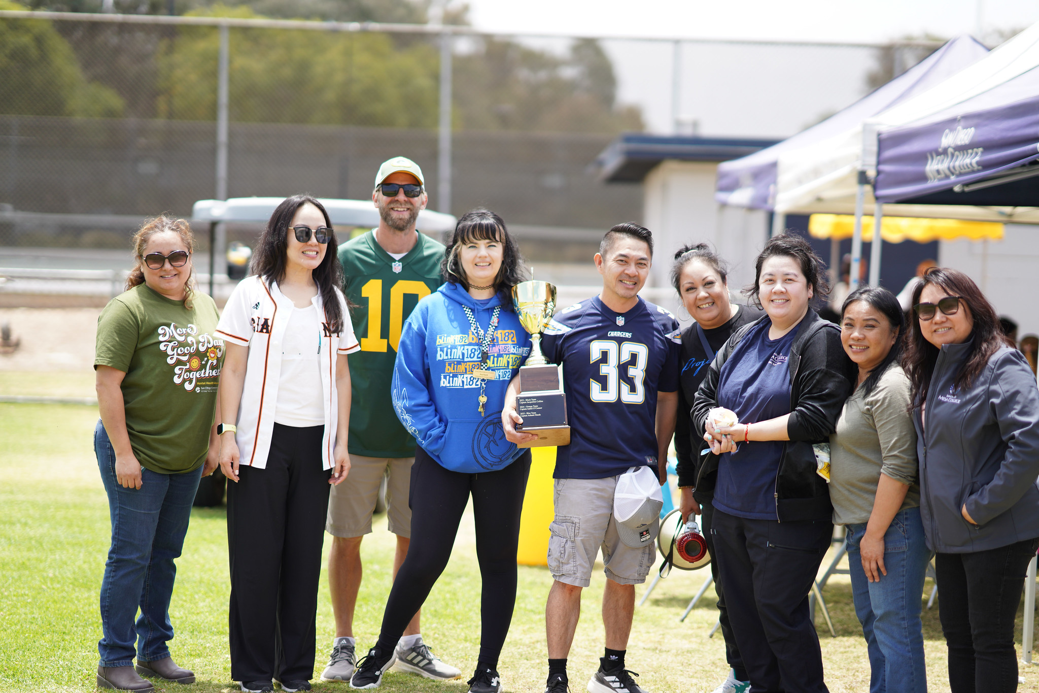 Nine employees on a grassy field holding a large trophy after a softball game.&nbsp;