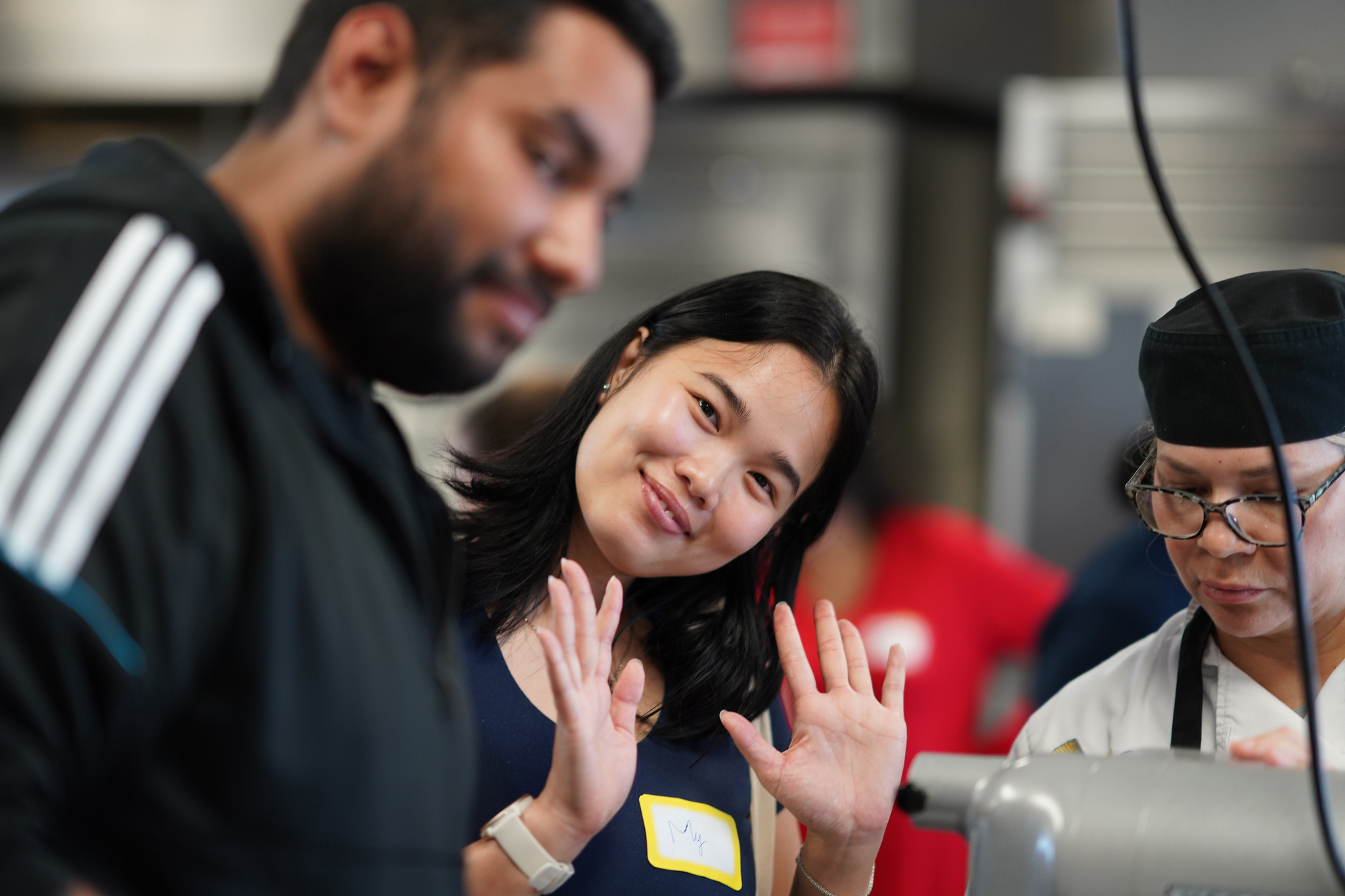 An employee at a Mesa&nbsp; culinary station waves at the camera with both hands.