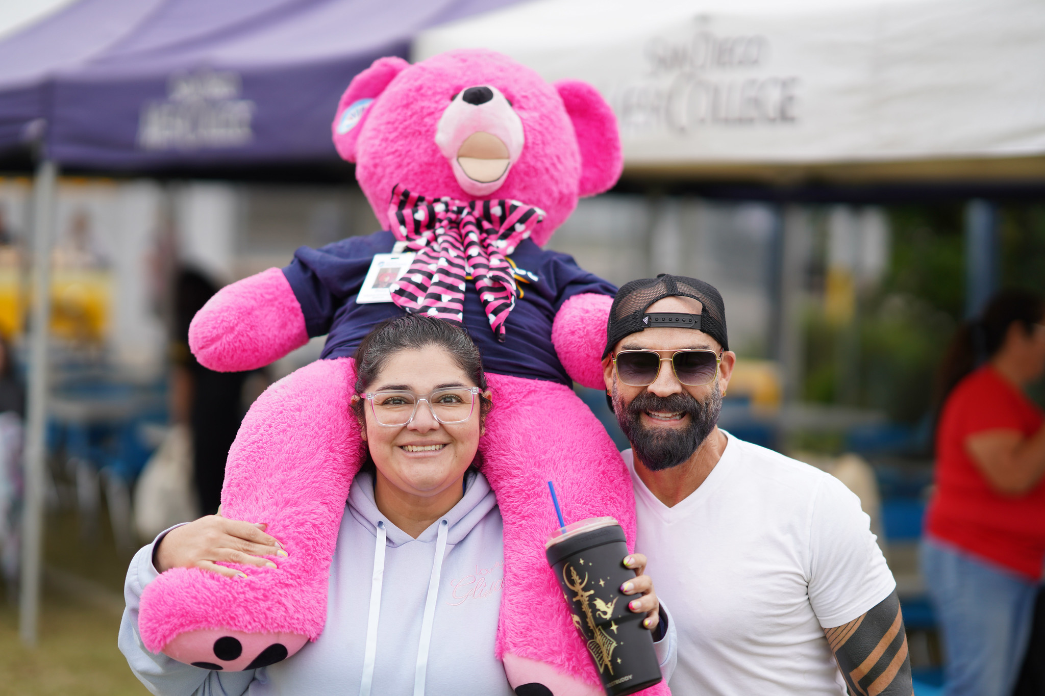 A man with a lady who has a giant pink bear on her shoulders.&nbsp;