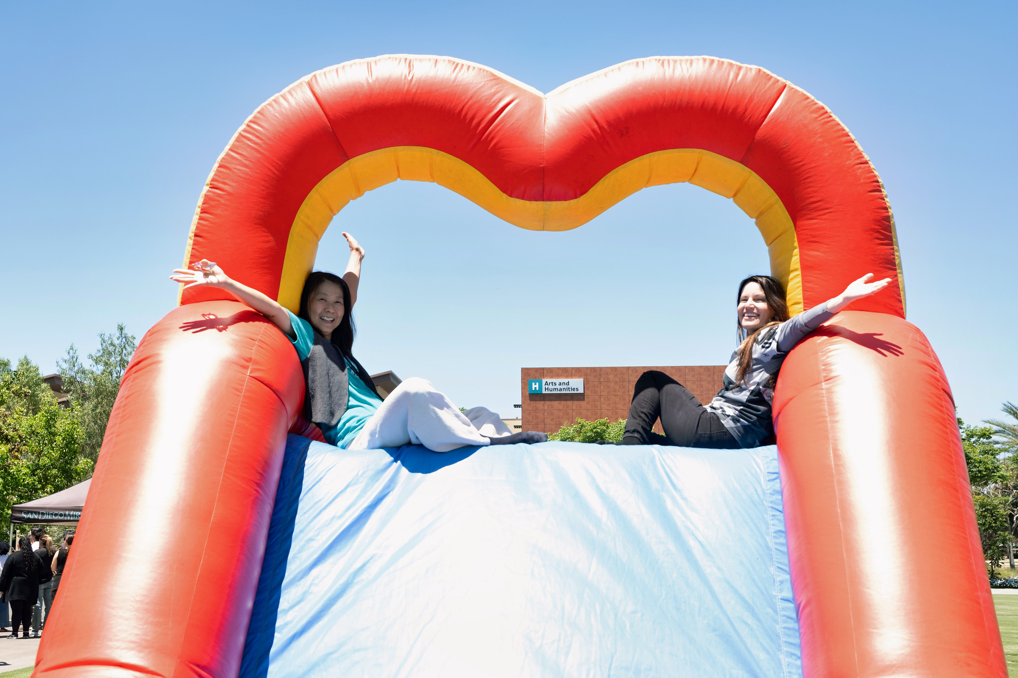 Two employees sit at the top of giant blow up slide.&nbsp;